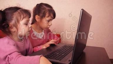孩子们在笔记本电脑里玩。 两个小女孩印在笔记本电脑上。 两个姐姐坐在橙色的沙发上看着一圈